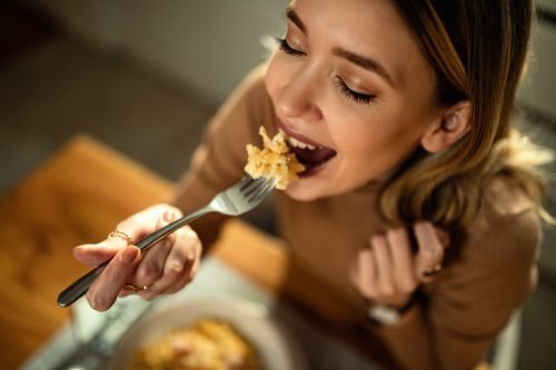 Close-up of happy woman eating pasta for dinner.