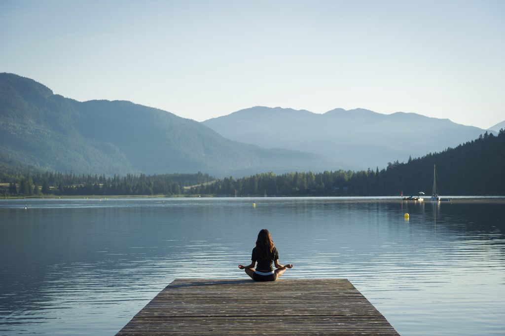 young woman in lotus position on dock over lake